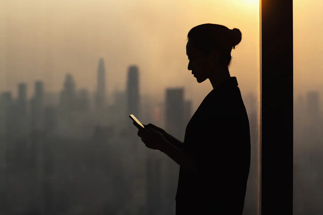 Silhouetted whistleblower looking at phone in front of city skyline, representing confidential communication with a whistleblower protections attorney.