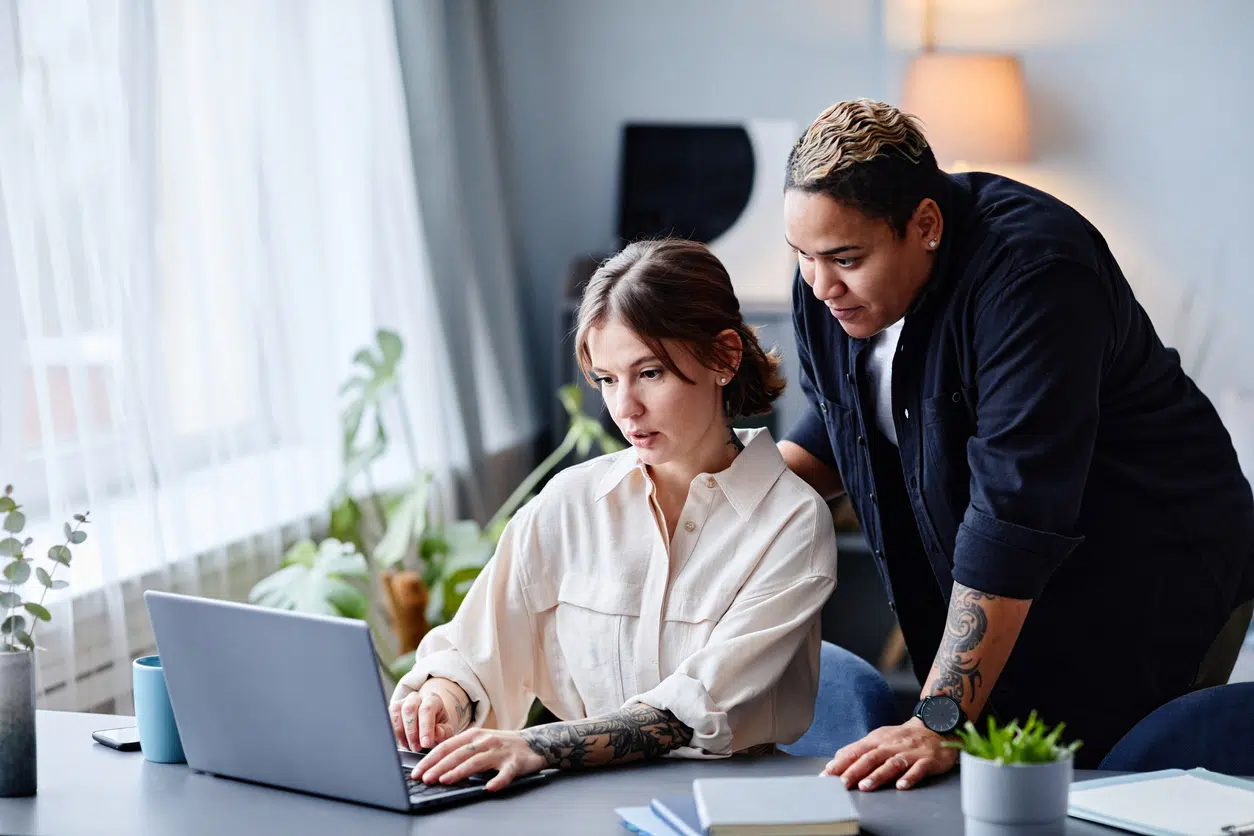 Two colleagues working together on a laptop in a well-lit office, symbolizing workplace collaboration and inclusivity.