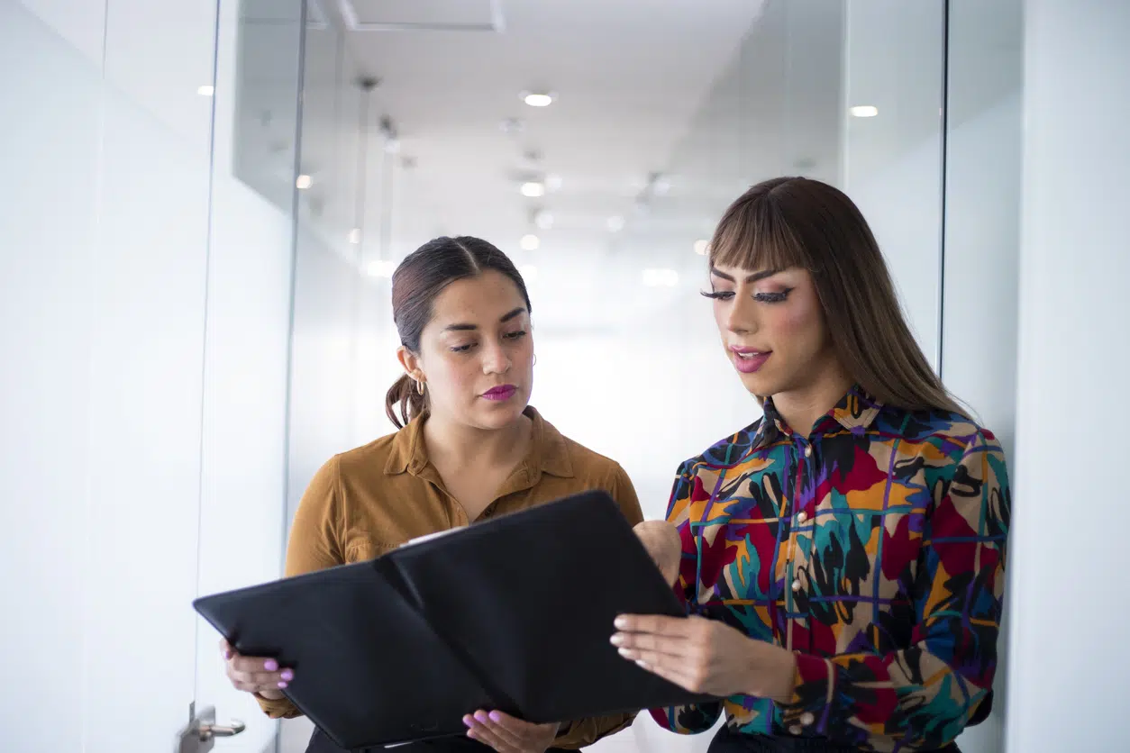 Two professional individuals reviewing a document together in a modern office setting, representing workplace inclusion and diversity.