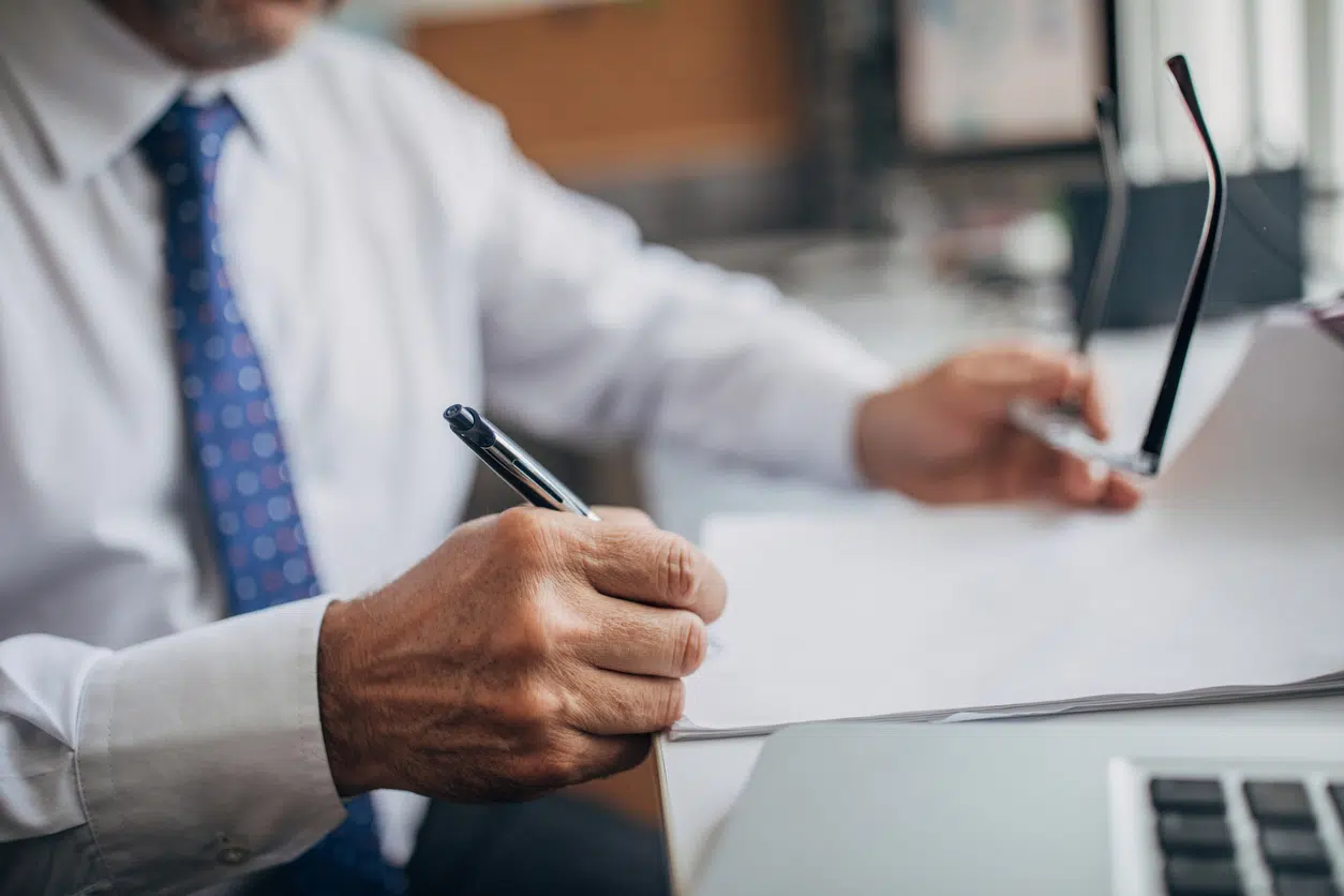 Close-up of a professional man in a white shirt taking notes on a document during a workplace discrimination or retaliation consultation.
