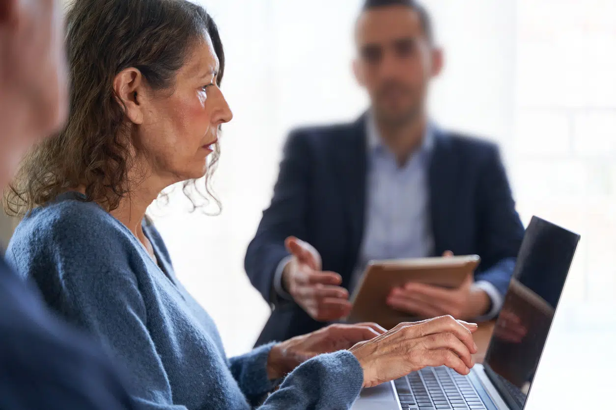 Older woman attentively listening during a meeting while a younger male colleague gestures in discussion — age discrimination in workplace.