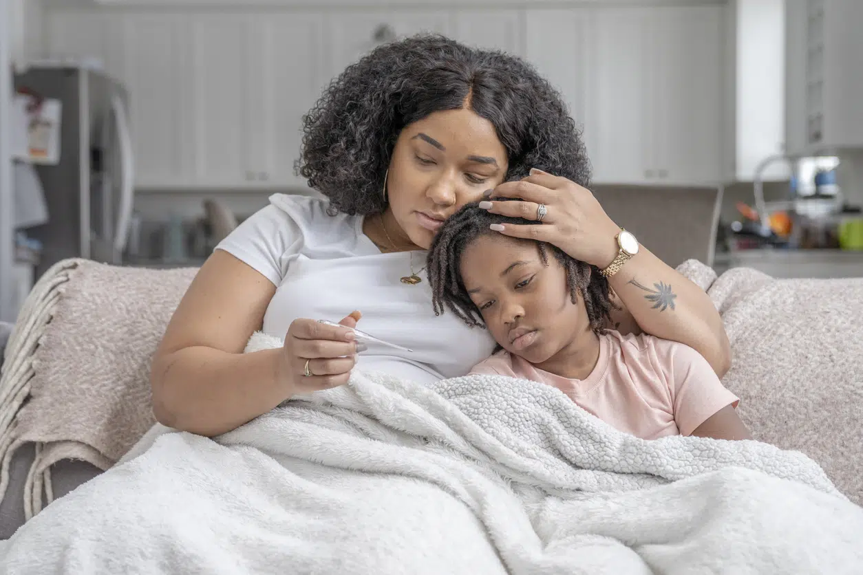 Mother comforting her sick child while checking their temperature at home, representing family medical leave protections.